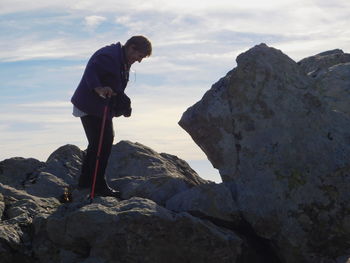 Side view of man standing on rock against sky