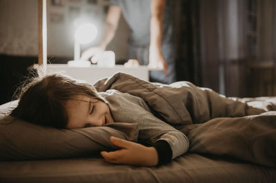 Happy boy sleeping on bed with father in background turning off light