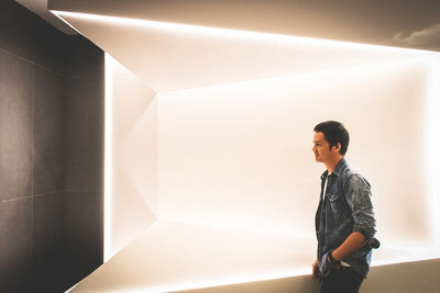 Side view of young man looking away against wall