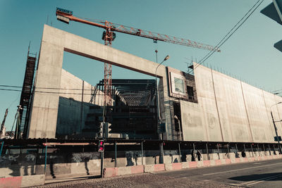 Low angle view of crane by building against sky