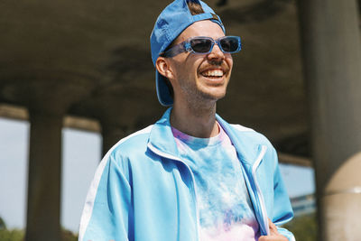 Happy young man in casuals wearing cap and sunglasses