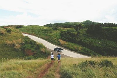 Rear view of men walking on road amidst field against sky