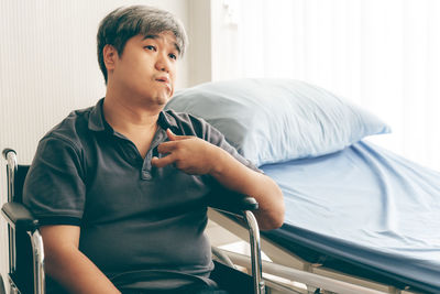 Young man looking away while sitting on bed