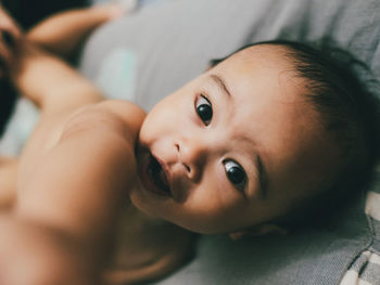 Close-up of cute baby boy looking at the camera lying on bed at home