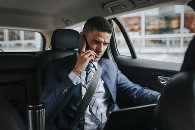 Businessman talking on smart phone while sitting with laptop in car