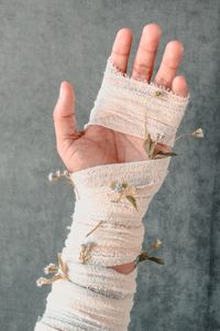 Cropped hand of person with bandage and dry flowers against wall