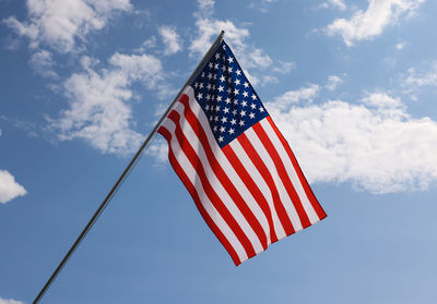 Us national flag hanging on flagstaff over cloudy blue sky, symbol of american patriotism