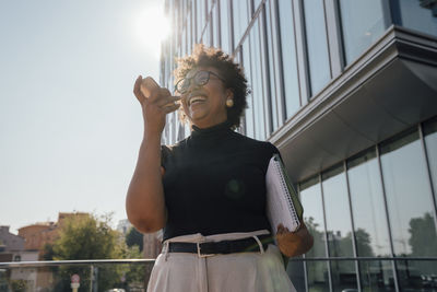 Happy businesswoman holding note pad talking on smart phone through speaker