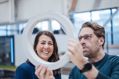 Happy businesswoman analyzing machine part with colleague in industry