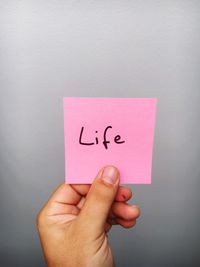 Cropped hand of person holding life text on adhesive note against gray background