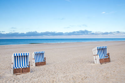 Hooded chairs on beach against sky