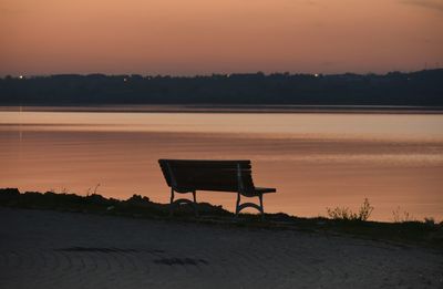 Empty chair on beach against sky during sunset