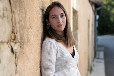 Portrait of young woman standing against wall