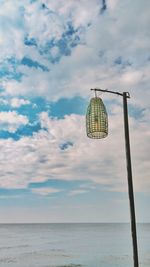 Low angle view of lighting equipment by sea against cloudy sky