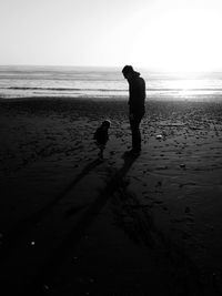 Rear view of father with dog walking on beach