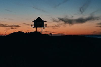 Silhouette house on land against sky during sunset