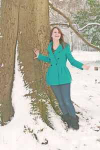 Portrait of smiling young woman standing by tree during winter