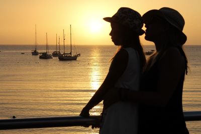 Woman with daughter by sea during sunset