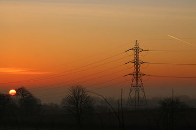 Low angle view of electricity pylon against orange sky