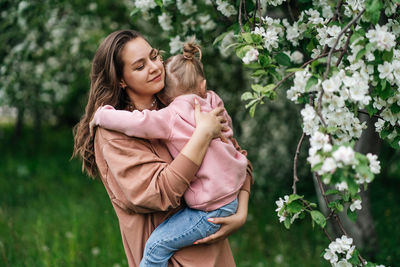 Young mother with her daughter in her arms in a blooming apple orchard