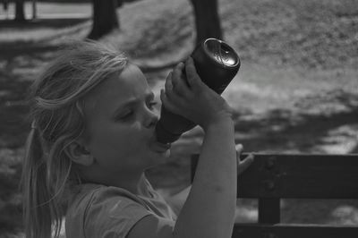 Side view of girl drinking from bottle outdoors