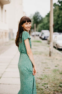 Portrait of a smiling young woman standing outdoors looking backwards 