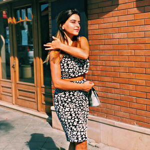 Young woman looking away while standing against brick wall