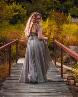 Rear view portrait of woman wearing evening gown while crossing footbridge against plants