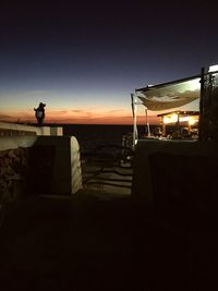 Silhouette built structure by sea against sky at night