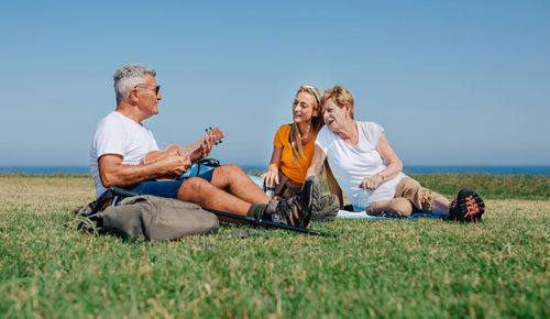 Friends sitting on field against clear sky
