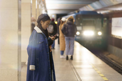 Japanese girl busy in cellphone at metro station with train arriving. young woman message to friend