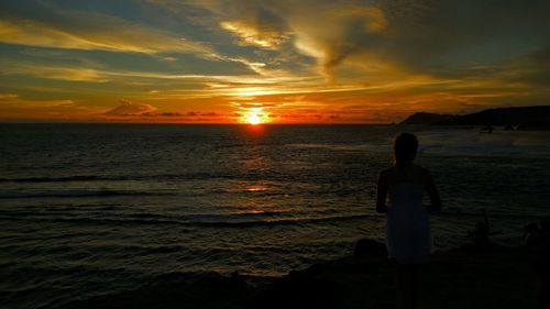 Silhouette woman standing on rock against sea during sunset