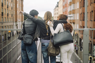 Rear view of male and female friends standing together near railing in city