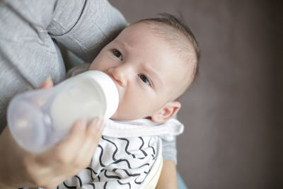 Midsection of mother feeding milk to baby boy with bottle at home