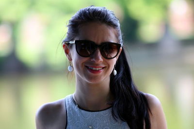 Portrait of smiling young woman wearing sunglasses against lake
