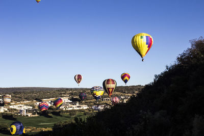 Hot air balloons flying over landscape against clear blue sky