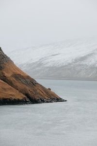 Scenic view of sea by snowcapped mountain against sky