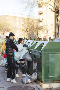 Young male and female environmentalists throwing waste in garbage can