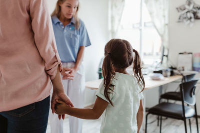 Girl holding hands of mother while female pediatrician explaining in doctor's office