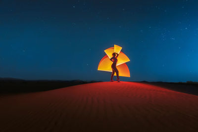 Full length of woman standing on sand dune against sky at night