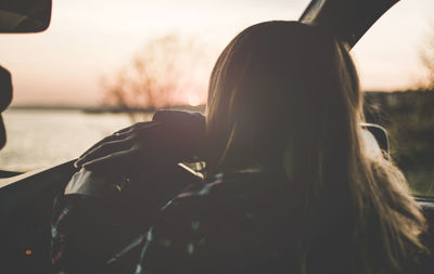 Rear view of woman driving car during sunset