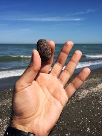 Close-up of hand by sea against sky