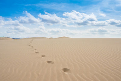 Footprints on sand in desert against sky