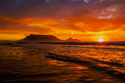 Scenic view of sunset over the sea, reflecting in the water  and table mountain in background. 