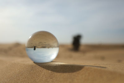 Close-up of ball on sand at beach against sky