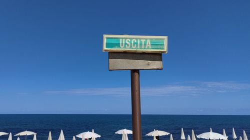 Information sign on wooden post by sea against blue sky