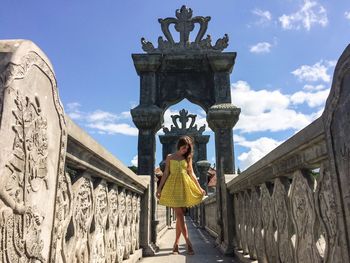 Full length of beautiful woman standing on stone bridge at tirta gangga against sky