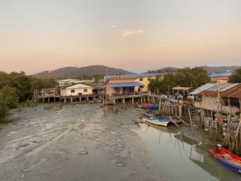 Boats moored in marina by houses against sky during sunset