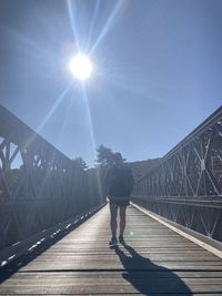 Rear view of man walking on footbridge against bright sun