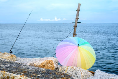 Colorful umbrella and fishing rod on shore against sky